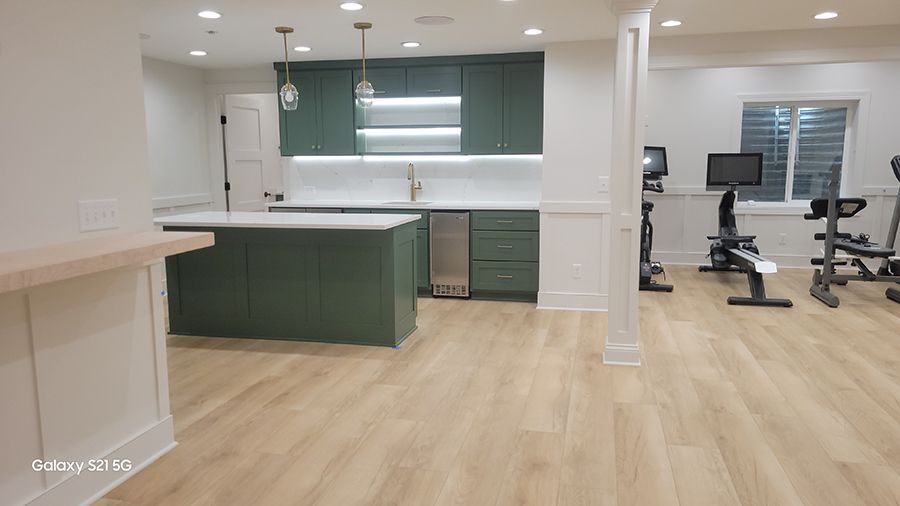 Modern basement with green cabinets, a kitchen, and home gym equipment.