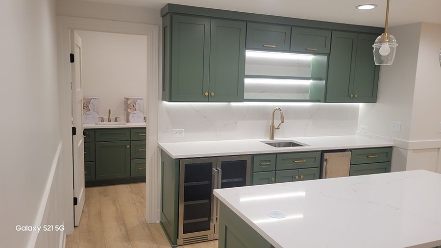 Green cabinets with white countertop and tile backsplash. Includes a sink, wine fridge, and open shelving.