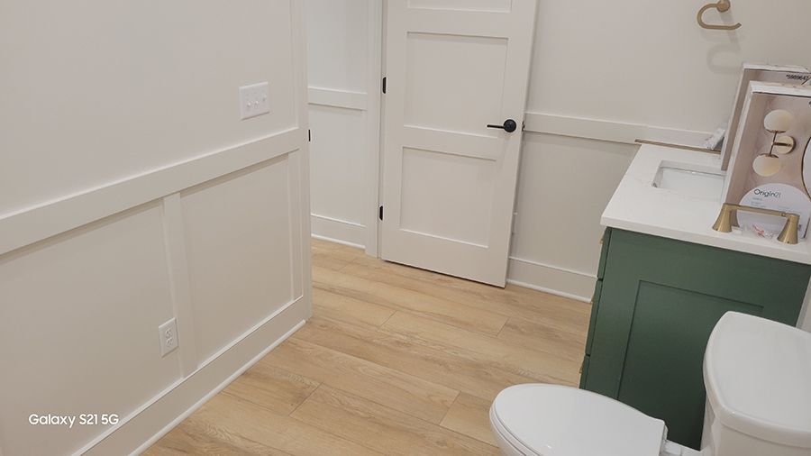 A modern bathroom with white walls, wood-look floor, green vanity, and a closed white door.