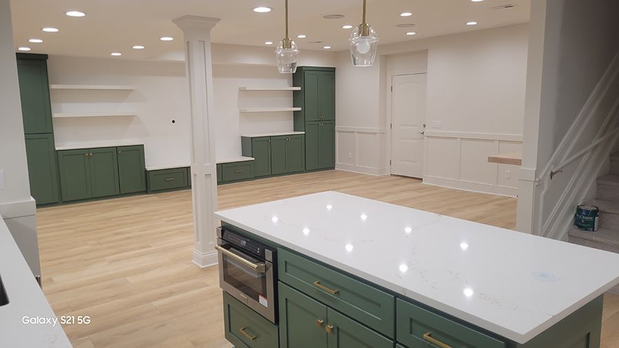 Kitchen with sage green cabinets, white countertops, island, and light wood flooring.