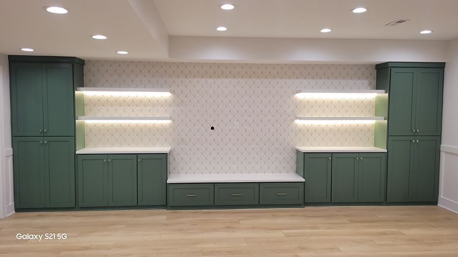 Green cabinets with built-in shelves and a bench against a patterned wall, lit by overhead lights.