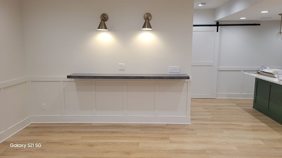 A room with a wall-mounted countertop, two sconce lights, and wood flooring.