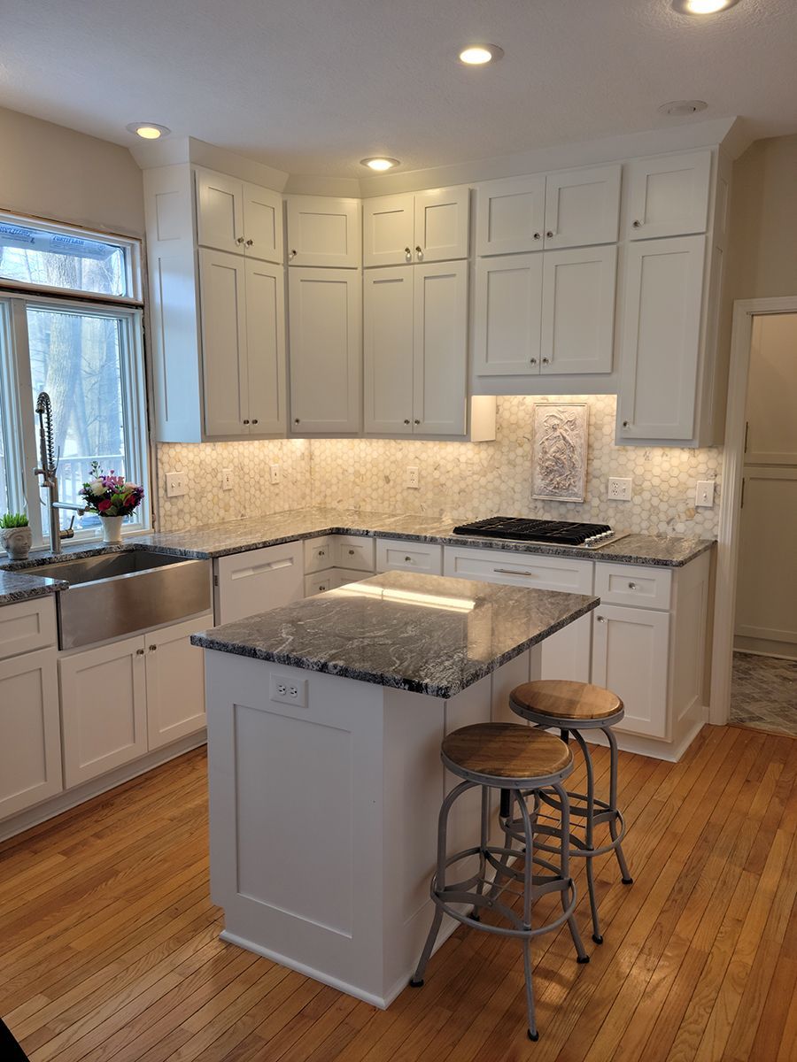 White kitchen with granite countertops, small island, wood floors, and recessed lighting.