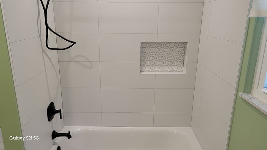 White tiled shower with black fixtures and built-in shelf.