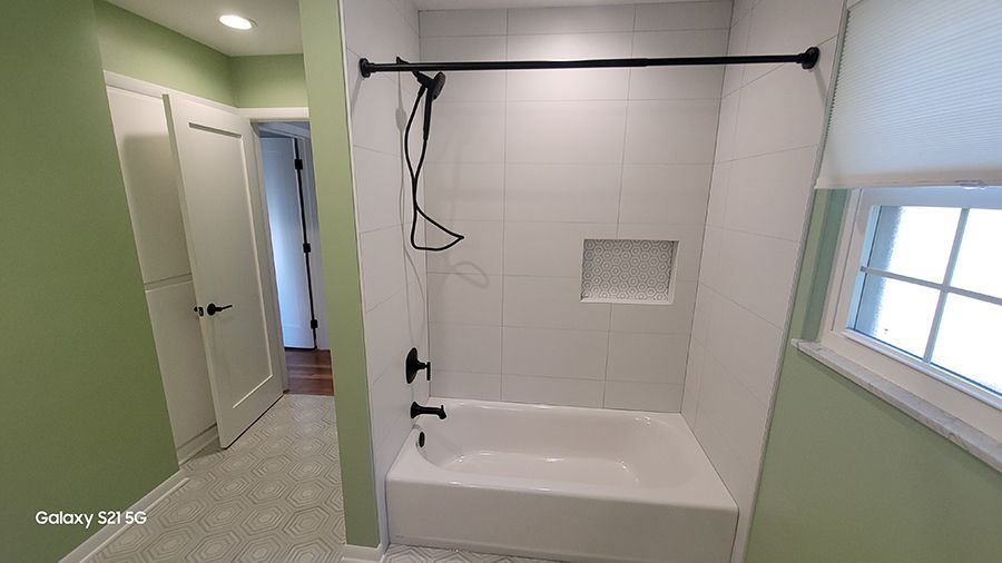 Bathroom with white tiled shower, black fixtures, and green walls.