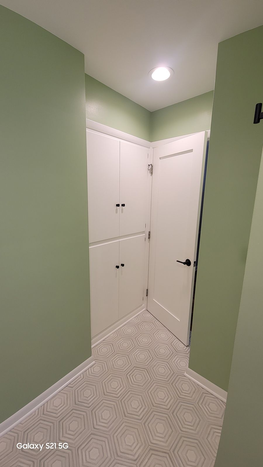 A hallway with sage green walls, white cabinets, and a patterned tile floor.