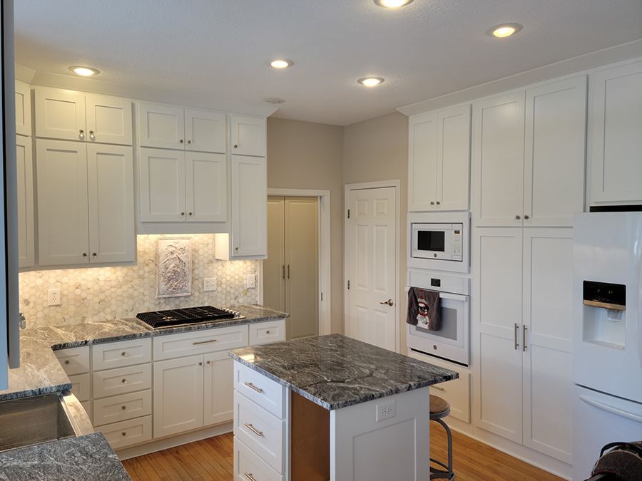 White kitchen with granite countertops, island, and appliances; light-colored wooden floors.