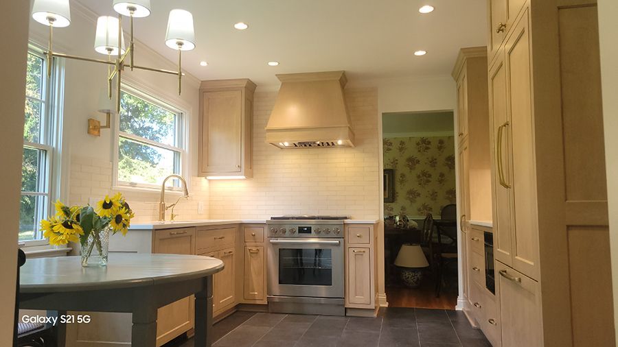 A kitchen with light-colored cabinets, stainless steel appliances, and a round table with sunflowers.