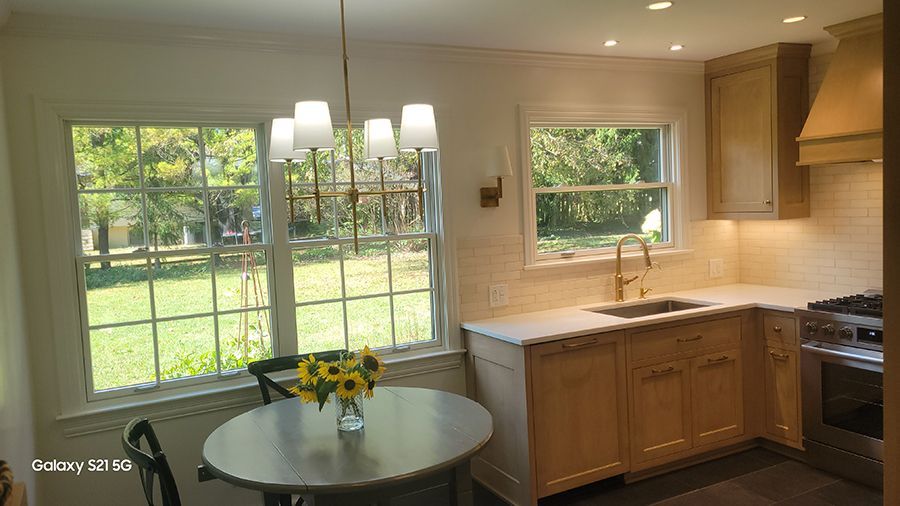 A bright kitchen with a table by windows, cabinets, and a stove.
