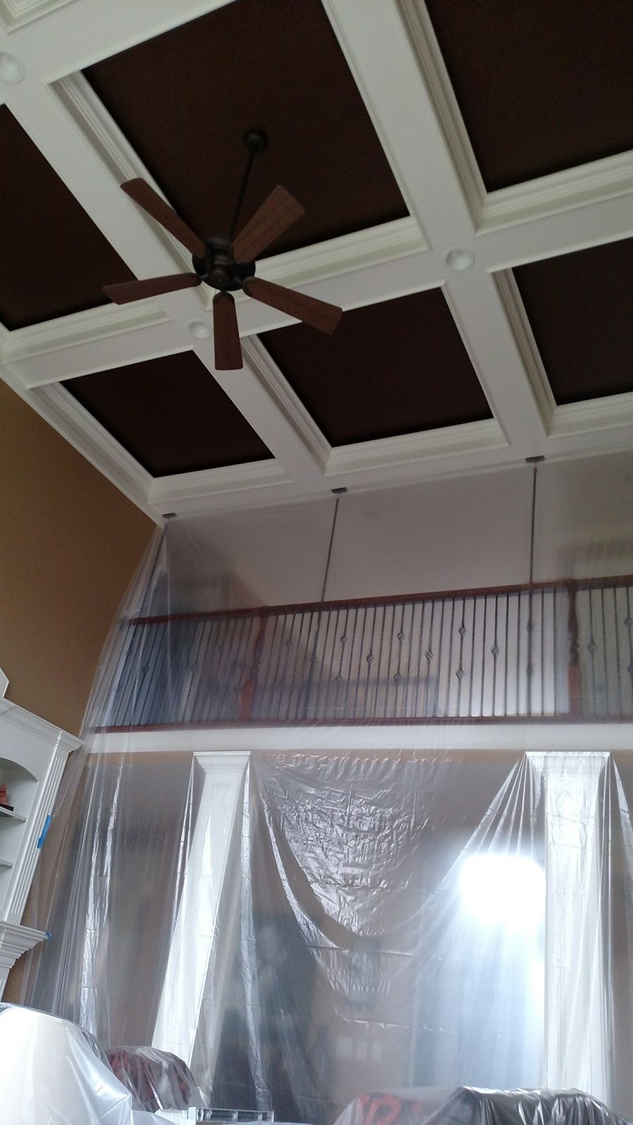 Room with brown ceiling panels, white beams, ceiling fan, and plastic sheeting.