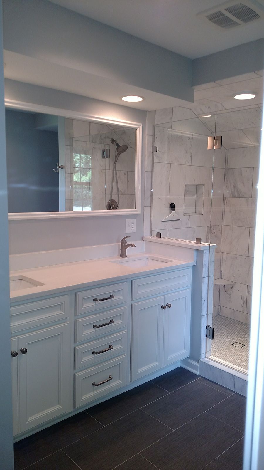 Bathroom with white vanity, marble tile shower, and dark tile floor.