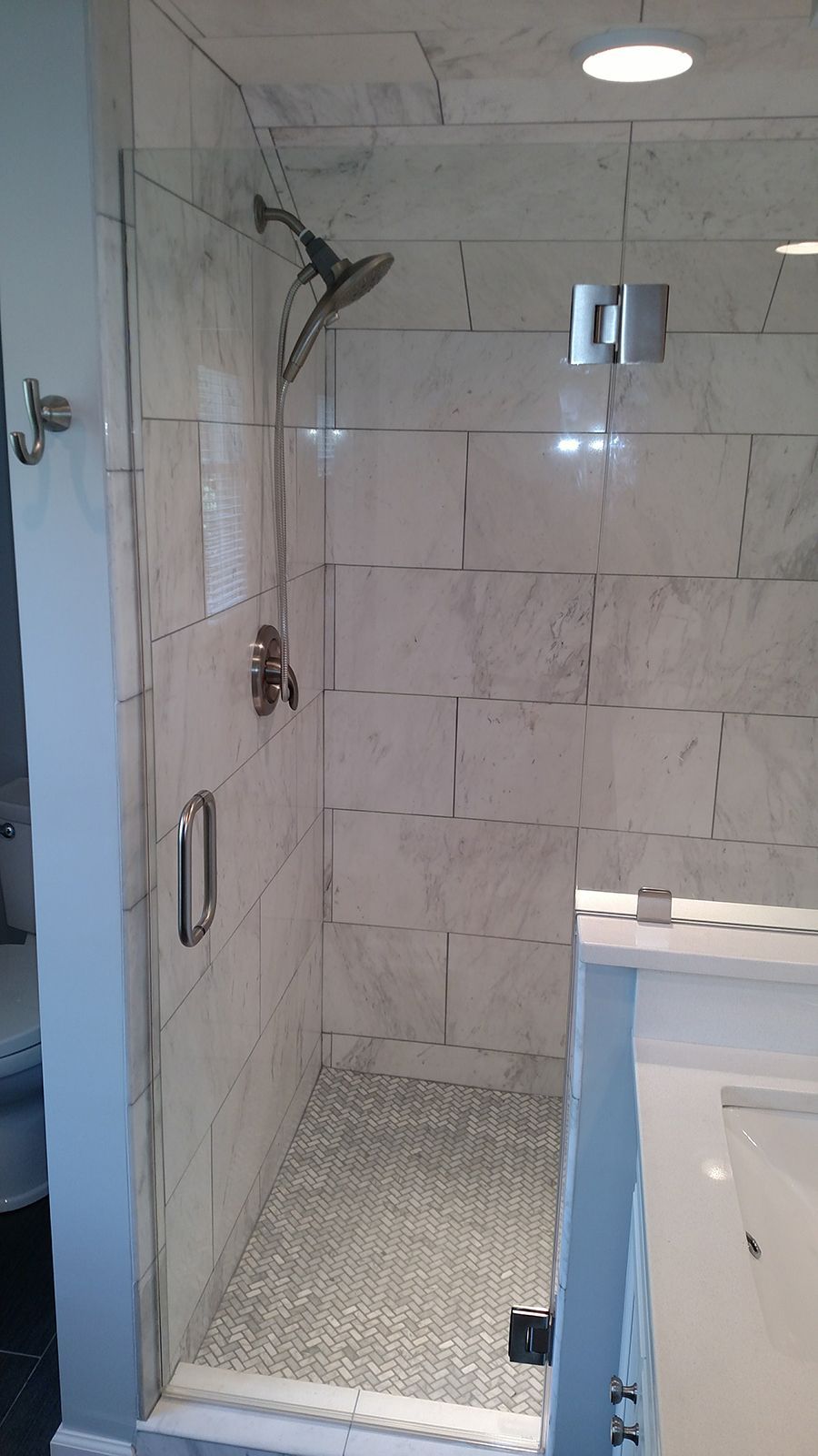Shower with glass door, marble tiles, silver fixtures.