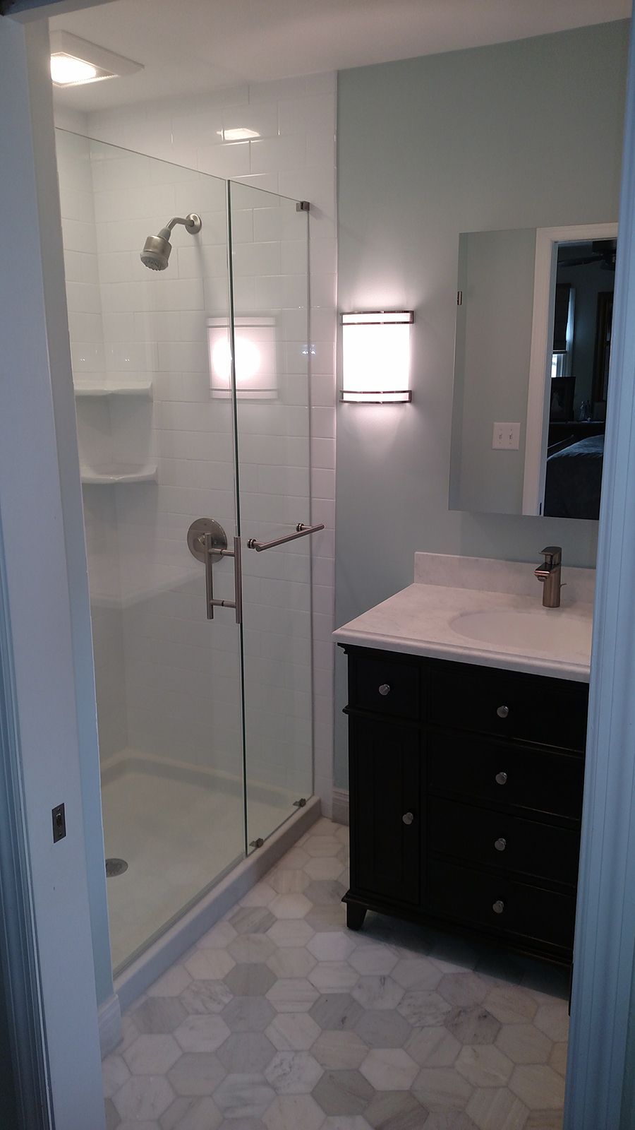 Bathroom with a glass shower, dark vanity, marble countertop, and hexagonal tile flooring.