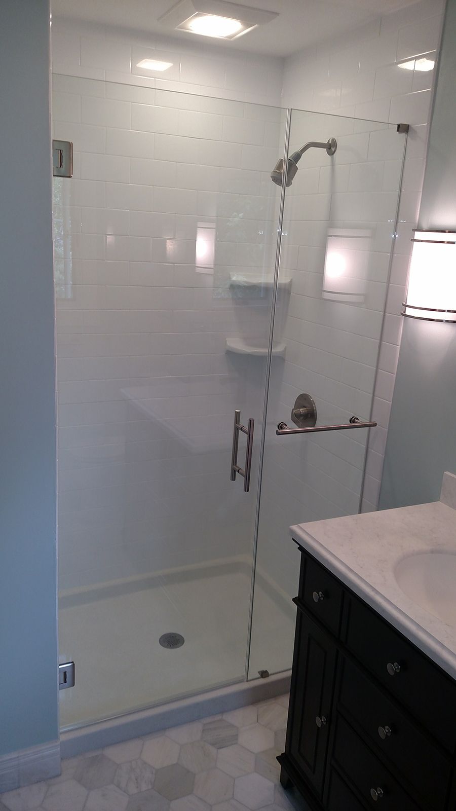 Shower stall with white tile, glass door, chrome fixtures, and a dark vanity.
