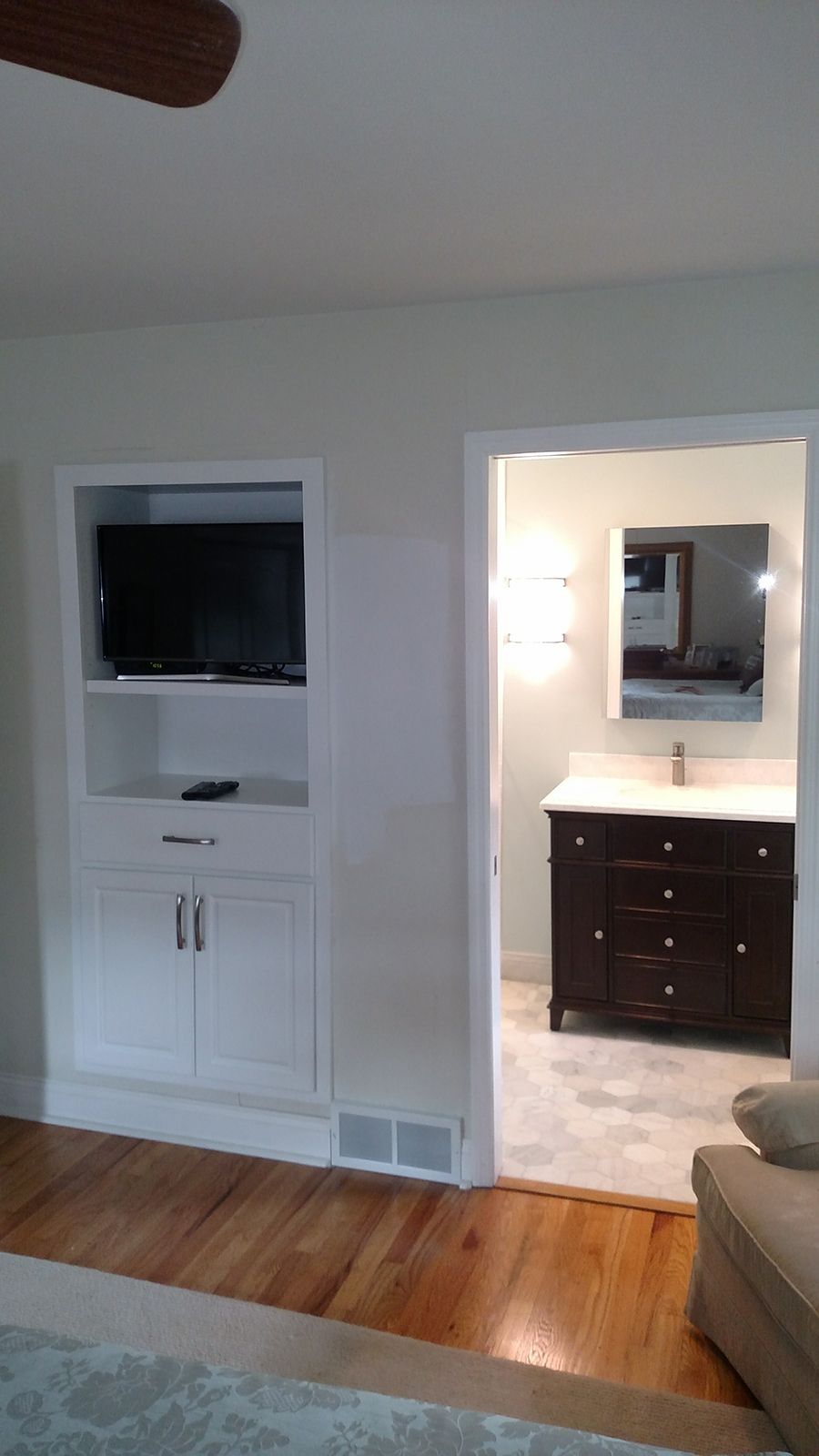 Built-in white cabinet with TV next to the open doorway to a bathroom with a dark brown vanity.