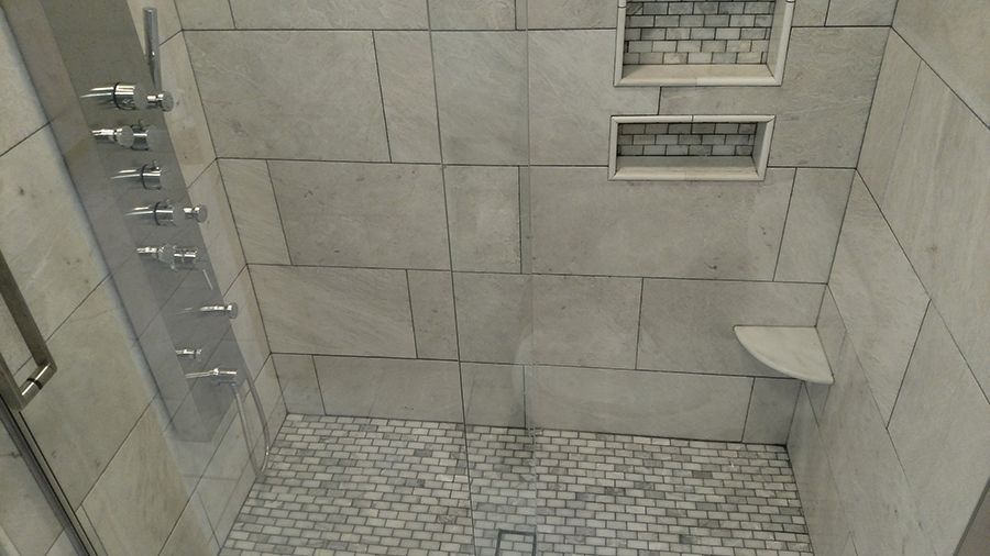 Modern shower interior with stone tile walls, built-in shelves, and multiple shower heads.