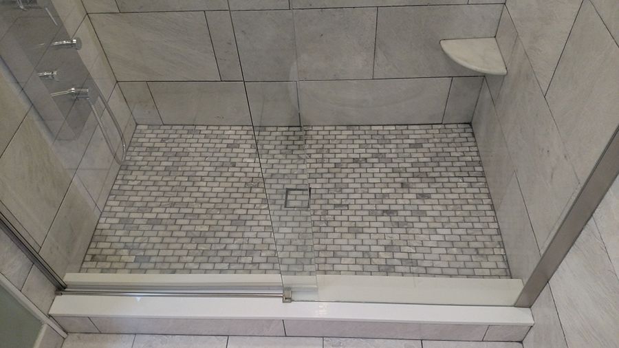 Shower with a white brick-patterned floor, gray walls, and a white ledge.