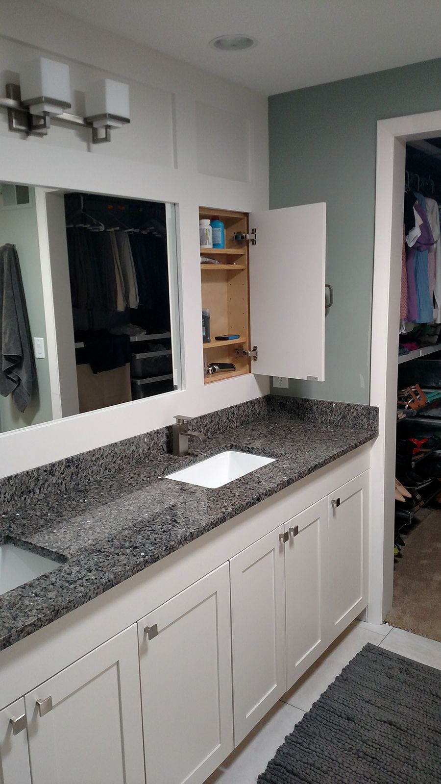 White bathroom vanity with granite countertop, mirror, and open medicine cabinet.