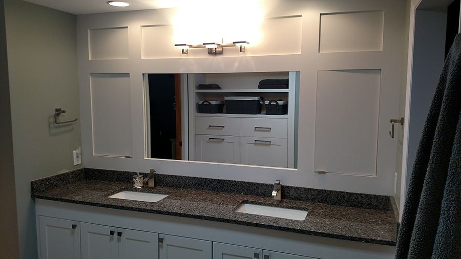 Bathroom vanity with mirror, lighting, double sinks, granite countertop, and white cabinets.