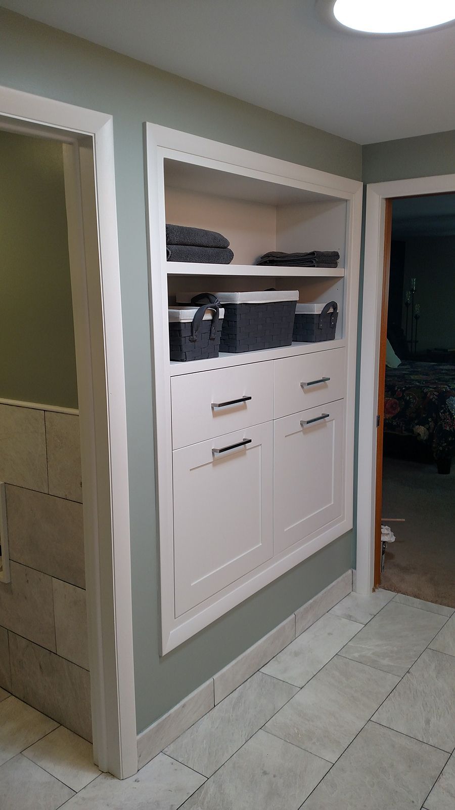 Built-in white storage cabinet with open shelves and drawers in a bathroom hallway.