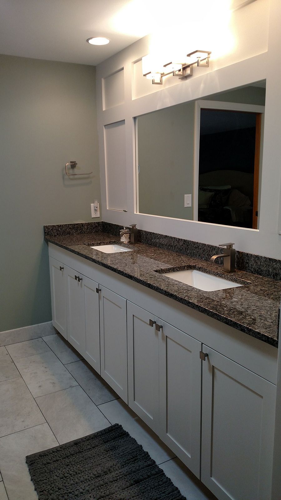Bathroom with double sink vanity, granite countertop, large mirror, and gray cabinets.