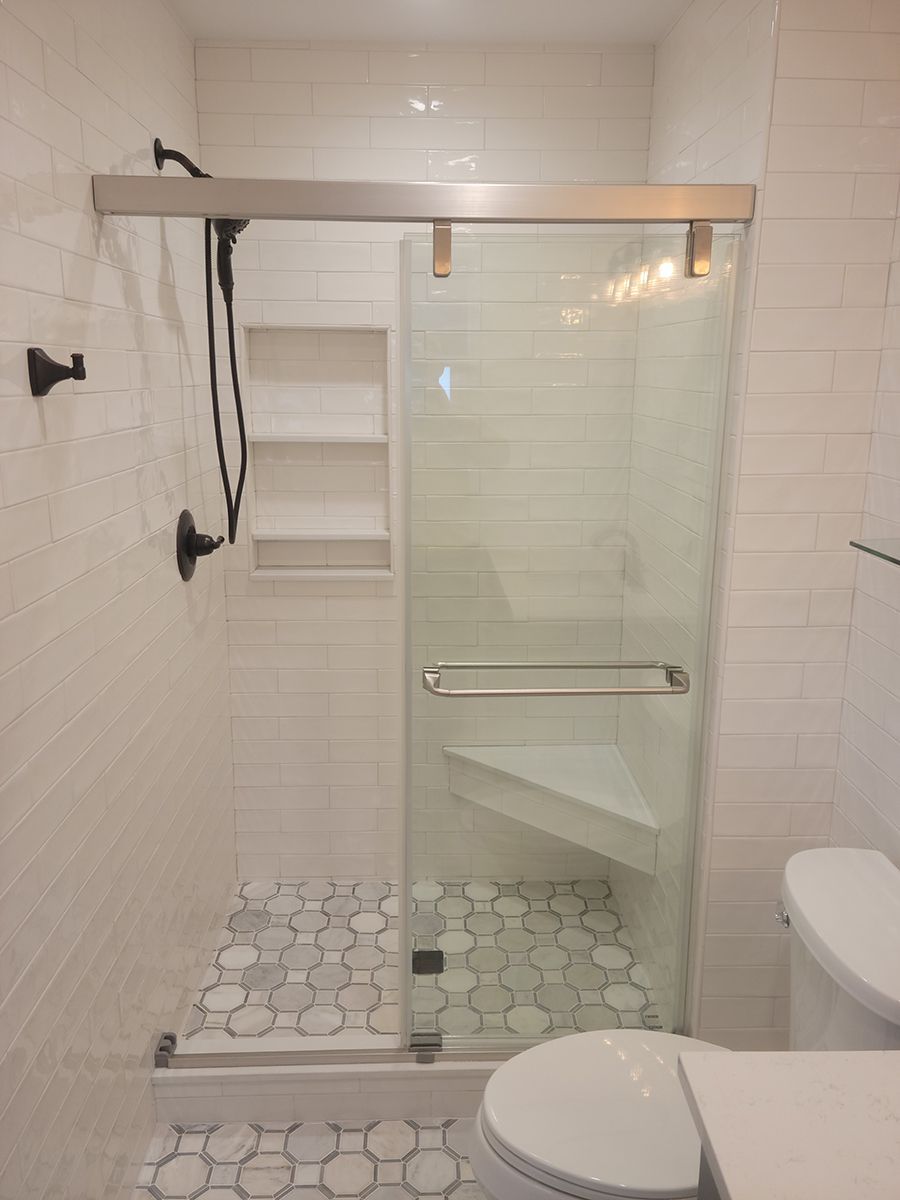Bathroom with glass shower door, built-in seat, white tile walls, and hexagon floor tiles.