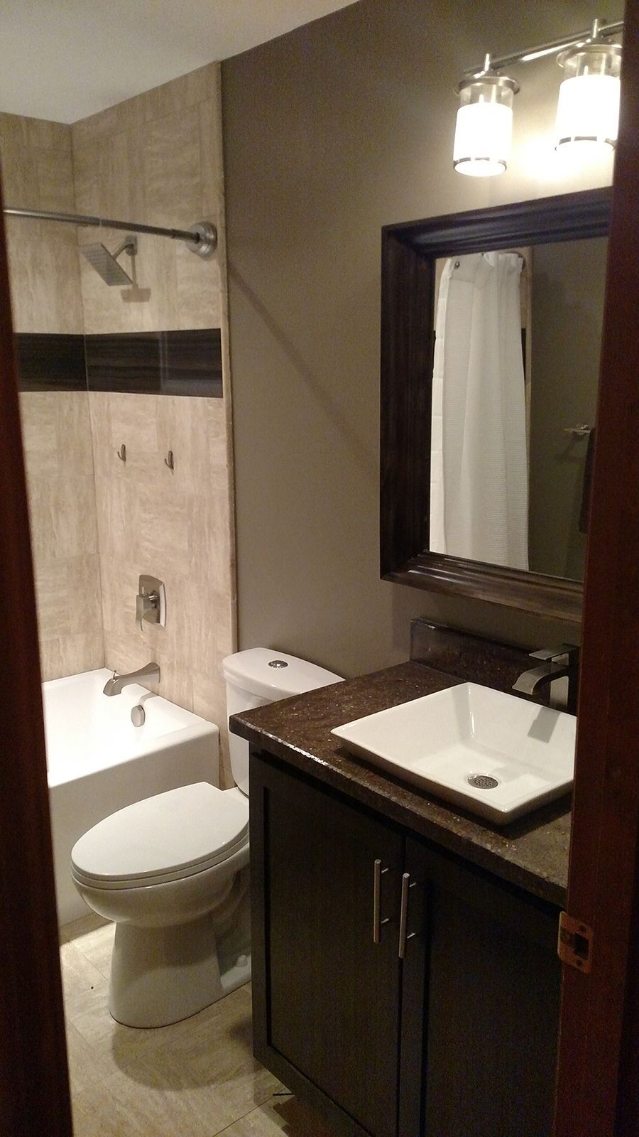 Bathroom with white tub and toilet, dark brown vanity, and a large mirror. Beige tile walls.