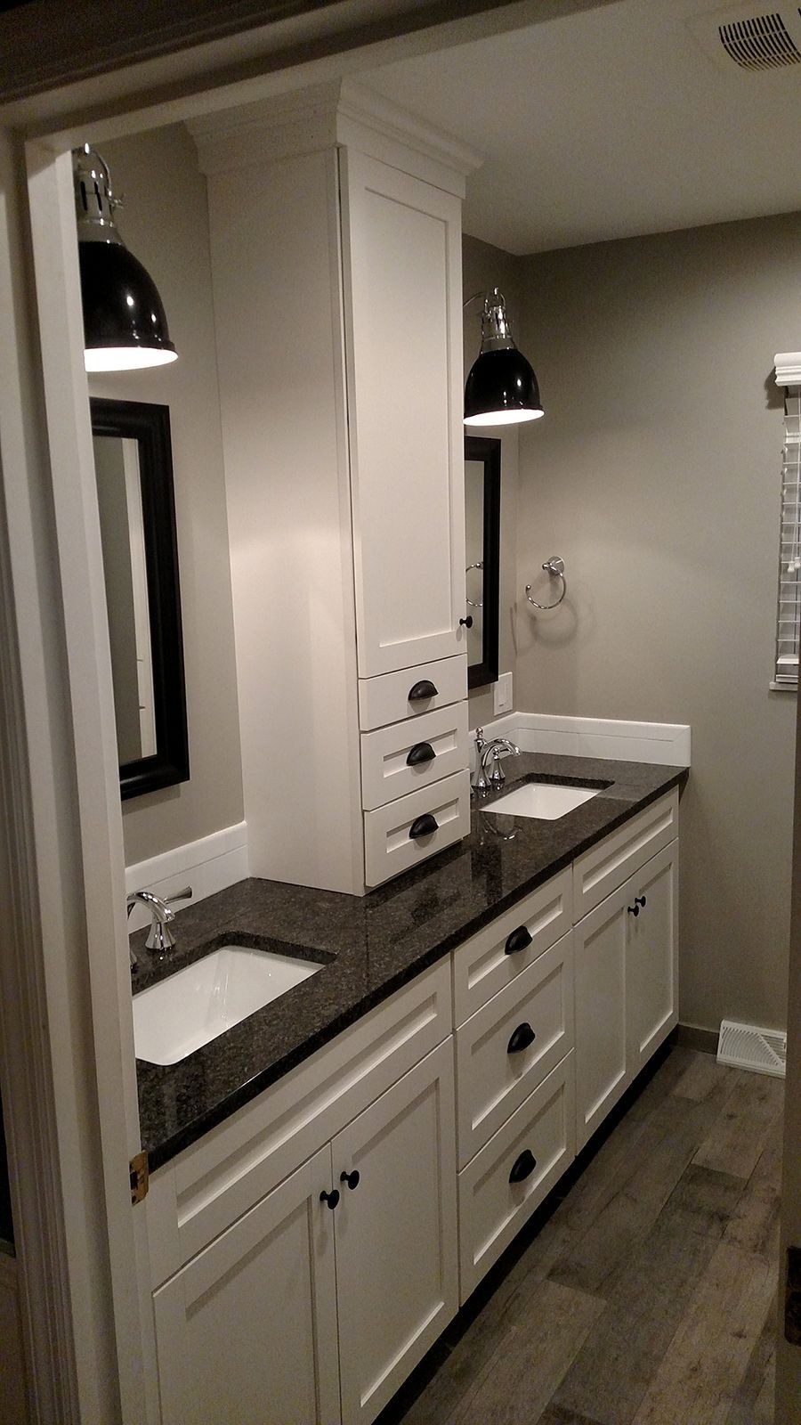 Bathroom with white cabinetry, black countertops, pendant lights, and two sinks.