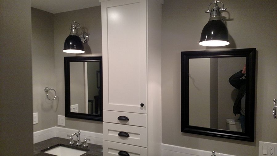 Bathroom with two black framed mirrors, white cabinets, and black pendant lights.