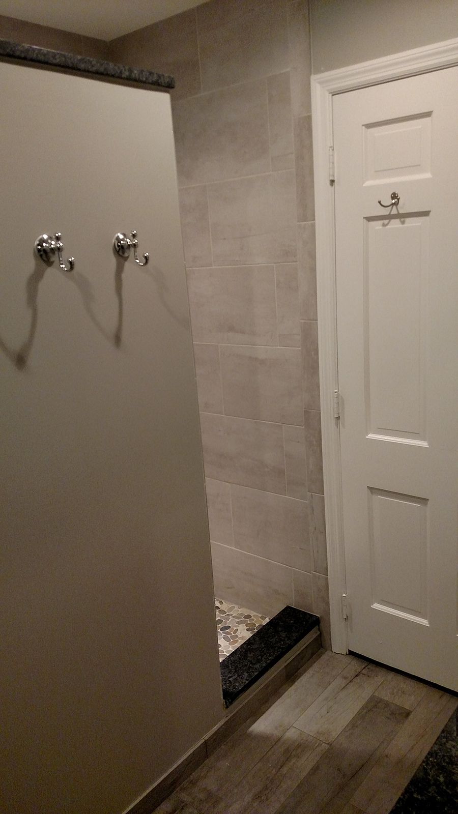 Shower stall with gray tile and a white door in a bathroom.