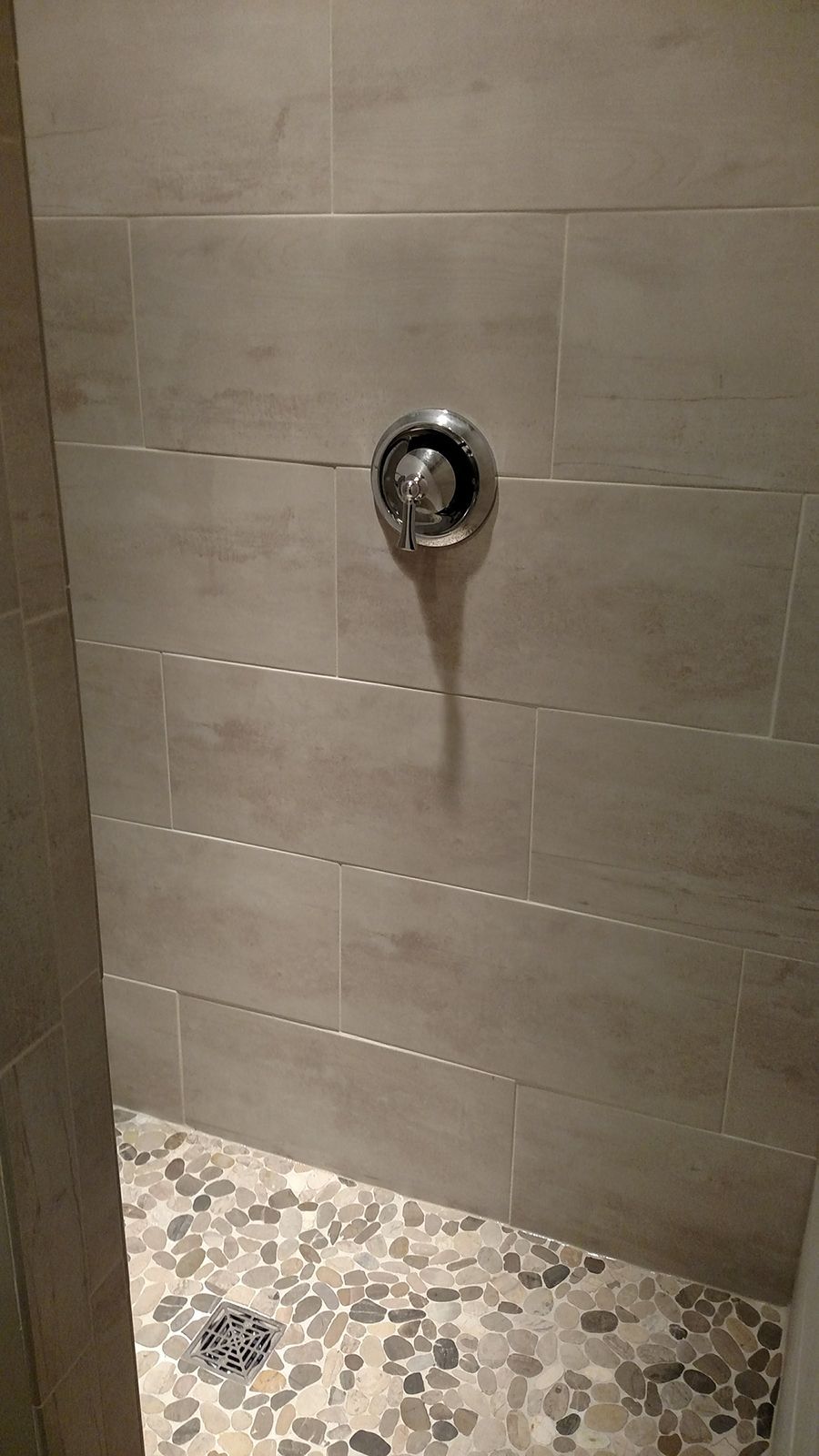 Shower with pebble floor, gray tiled walls, and silver showerhead.