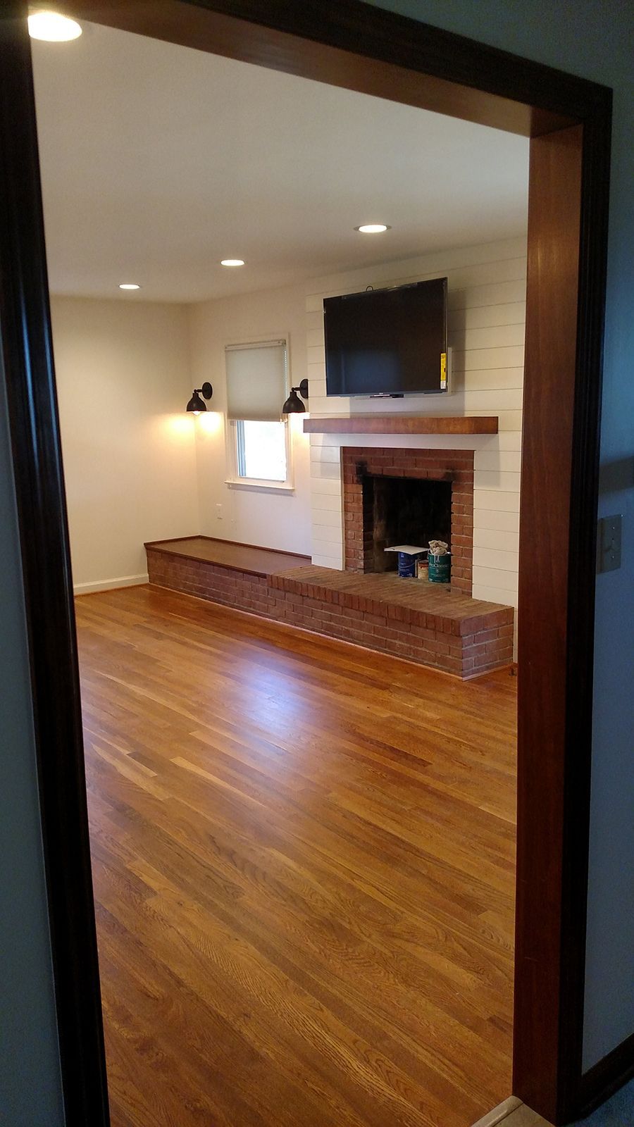 View of a living room with wooden floors, brick fireplace, and built-in bench. Dark wood trim.