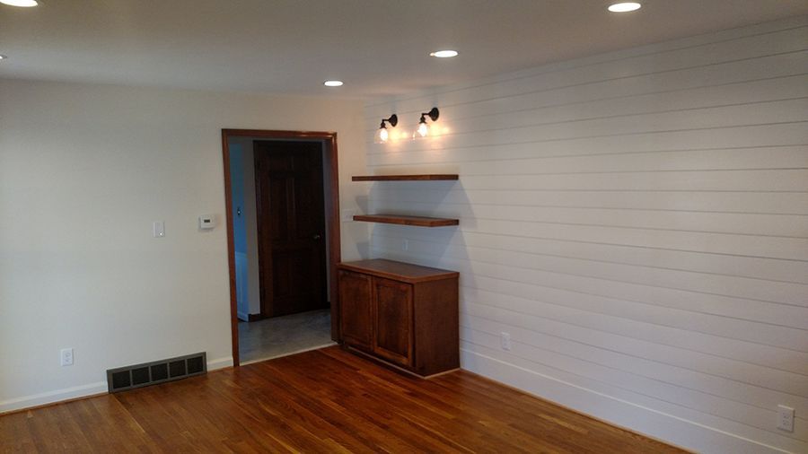 A room with wood flooring, white walls, built-in wooden cabinet and shelves, and a shiplap accent wall.