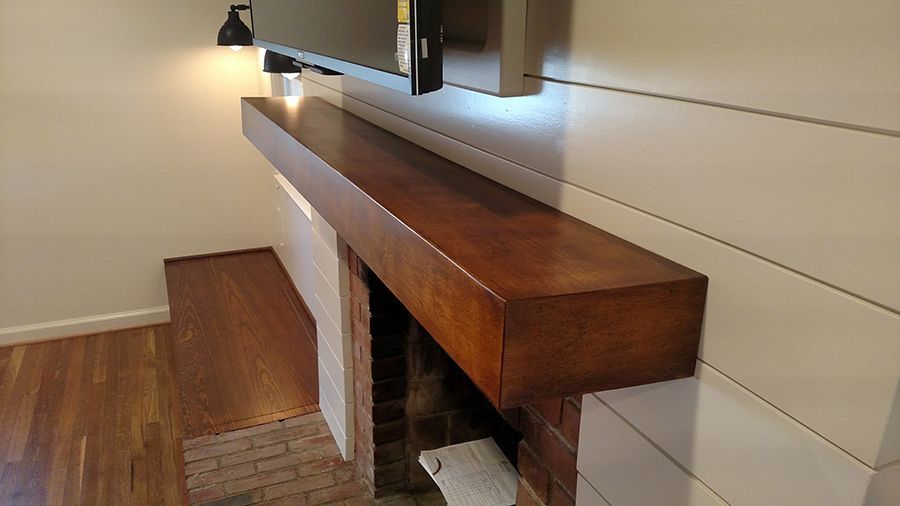 Wooden mantel above a fireplace with a mounted TV; shiplap wall.