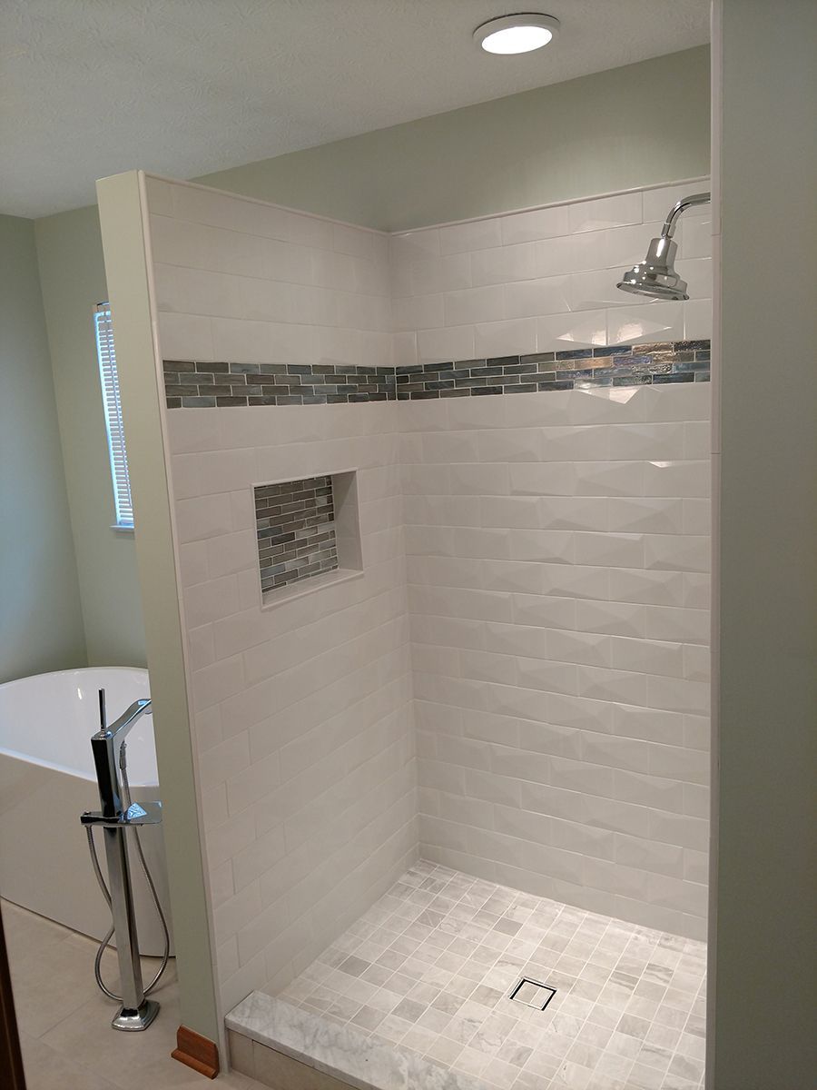 Modern shower with white tiled walls and a small mosaic accent, built-in niche, and gray tiled floor.