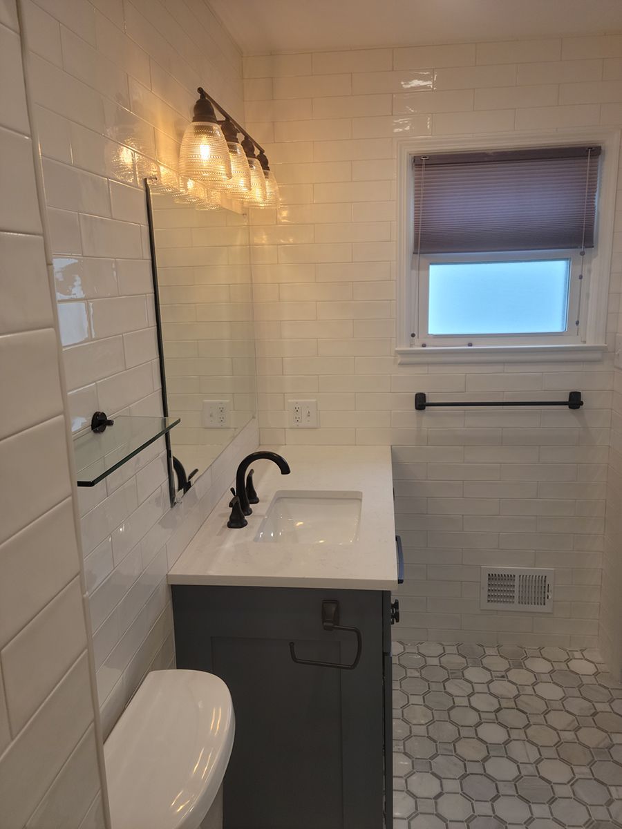 Bathroom with white subway tile walls, dark vanity, and window with a shade.