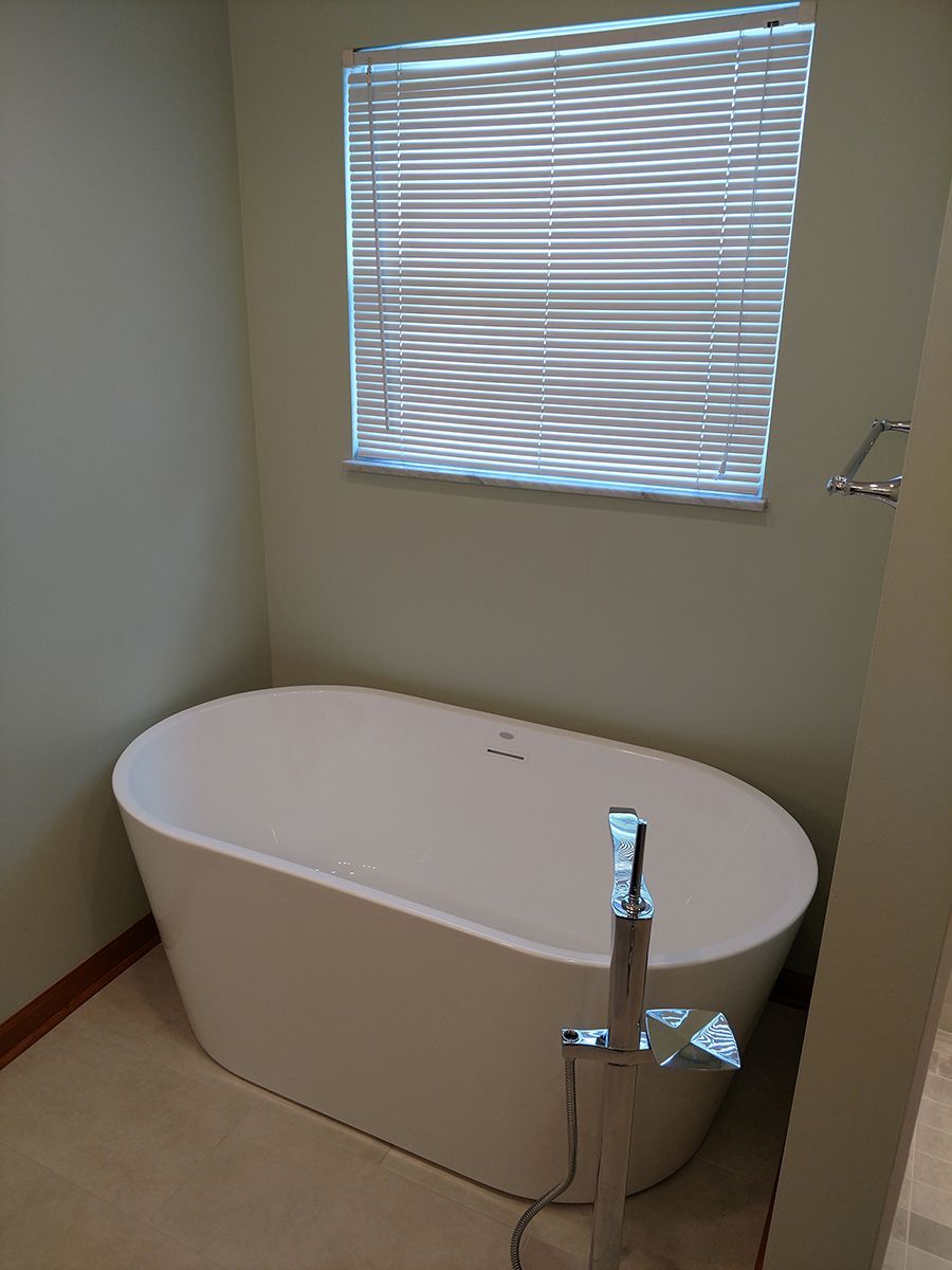 Freestanding white bathtub in a bathroom, near a window with closed blinds. Light green walls.