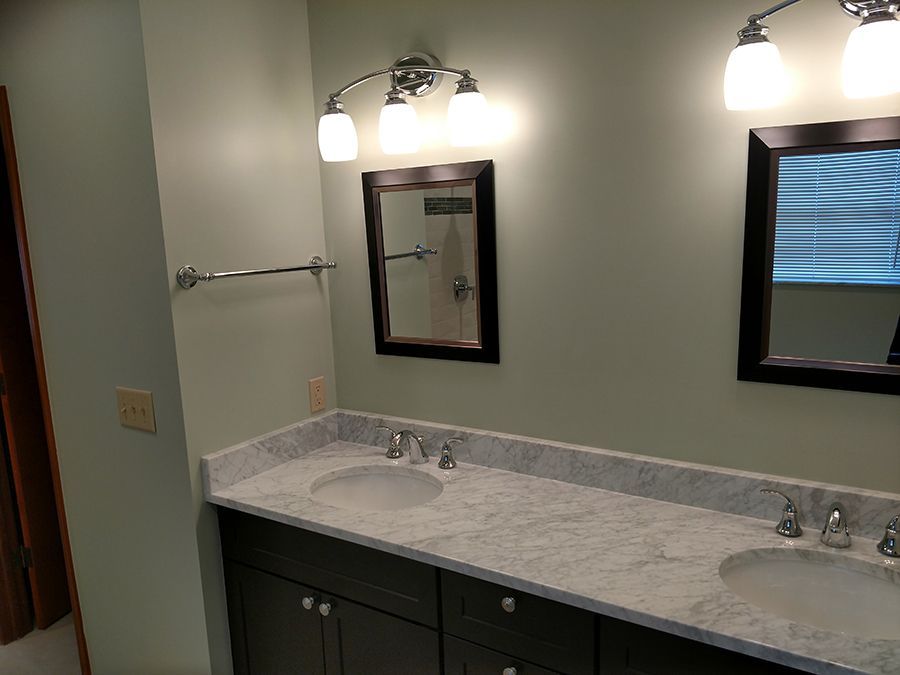 Bathroom with two sinks, two mirrors, and overhead lighting fixtures; light green walls.