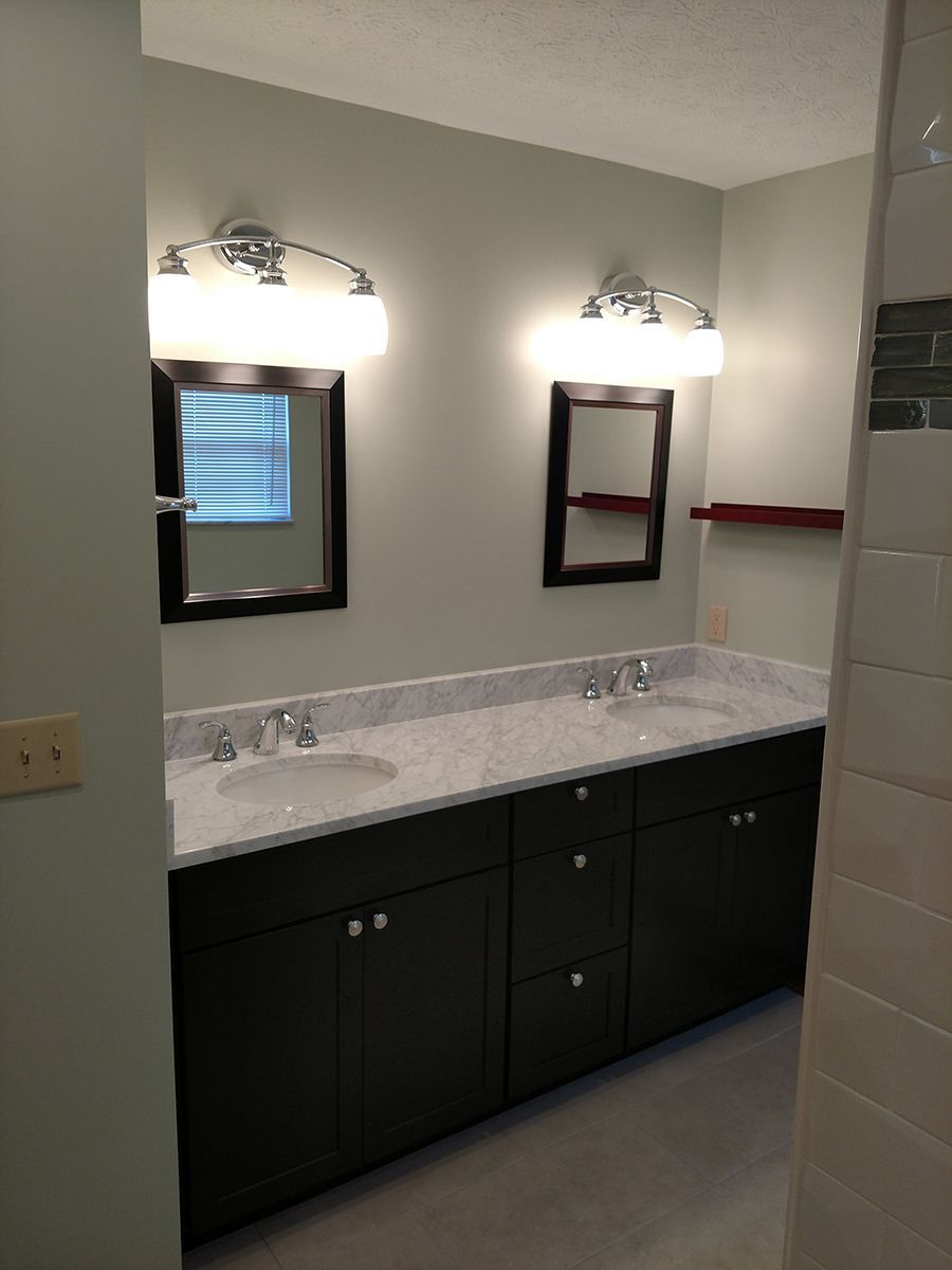 Bathroom with dark cabinets, marble countertop, and two mirrors with lighting.