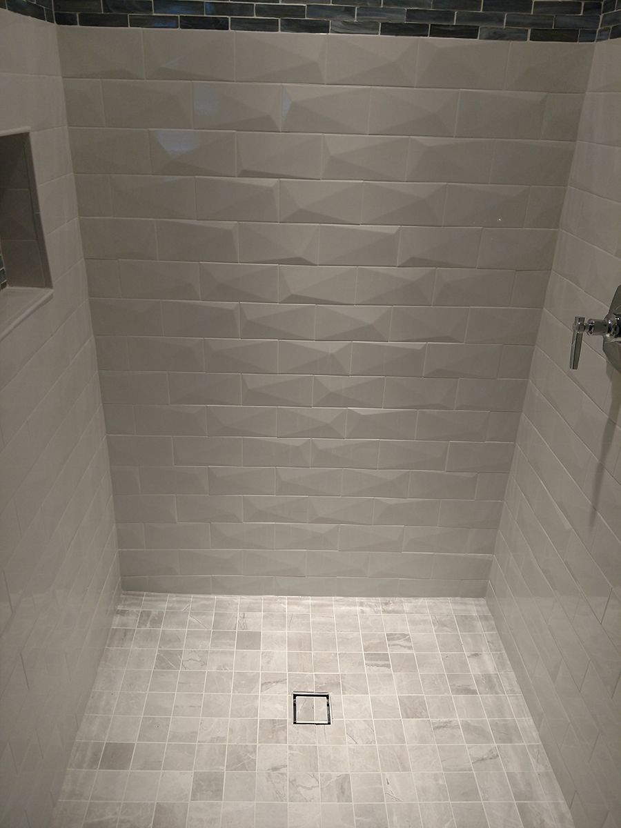 Tiled shower with light gray textured tiles on walls, smaller tiles on the floor, and a dark tile accent near the ceiling.