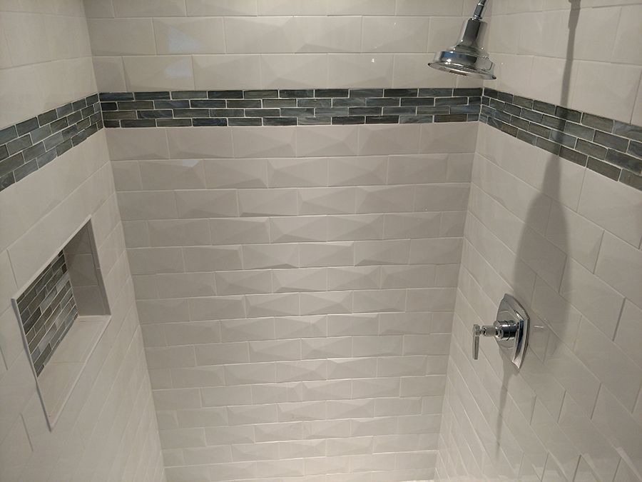 Tiled shower with a niche and accent band. Showerhead, faucet, and neutral color scheme.