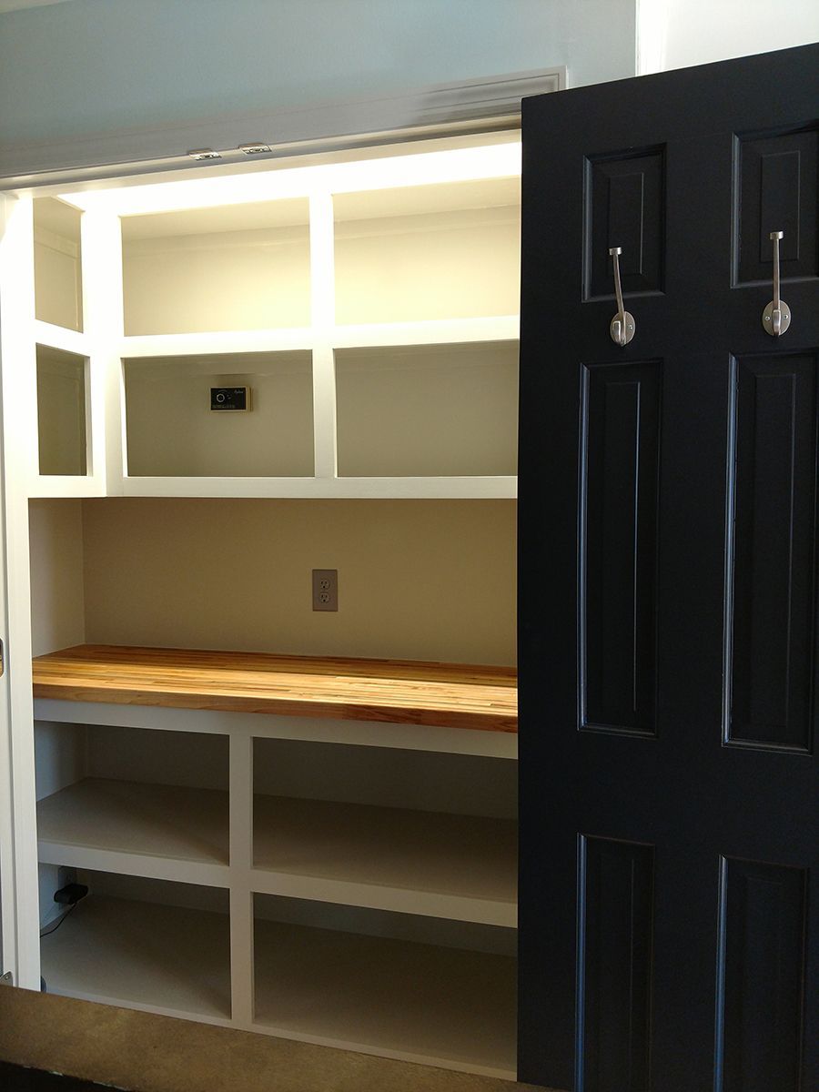 White pantry shelving with wooden countertop, open to reveal interior. Black door on right.