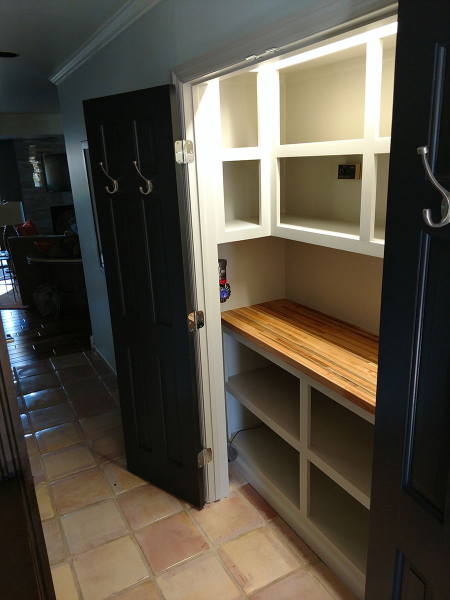 Open pantry with shelves and a butcher block counter; dark gray door with hooks.