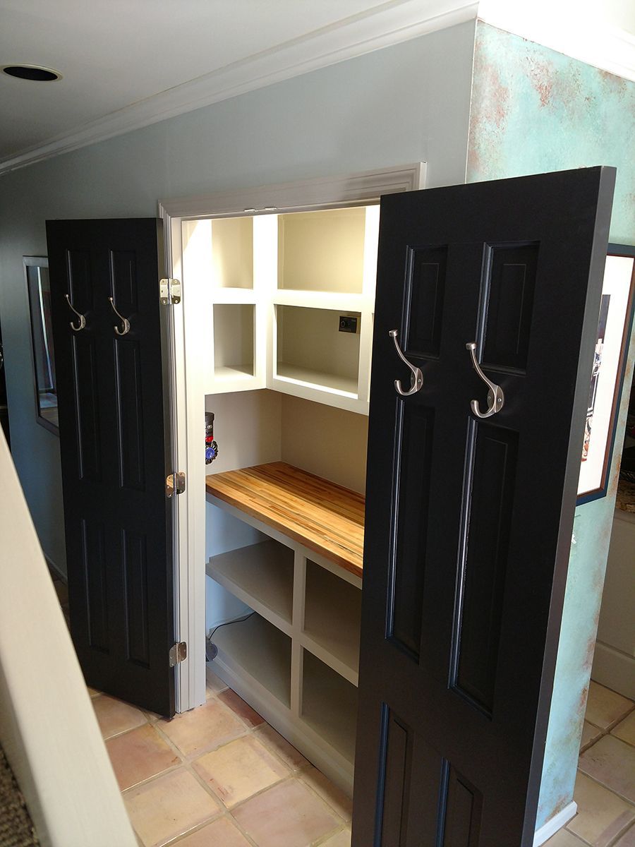 Pantry with black doors open, revealing shelves. Light wood counter. Beige tile floor. White and light blue walls.