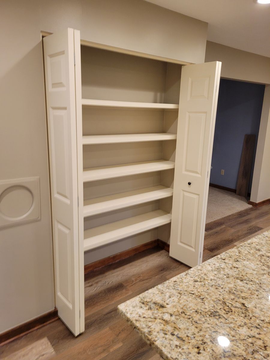 White pantry with six shelves, accessed by bi-fold doors, next to a granite countertop.