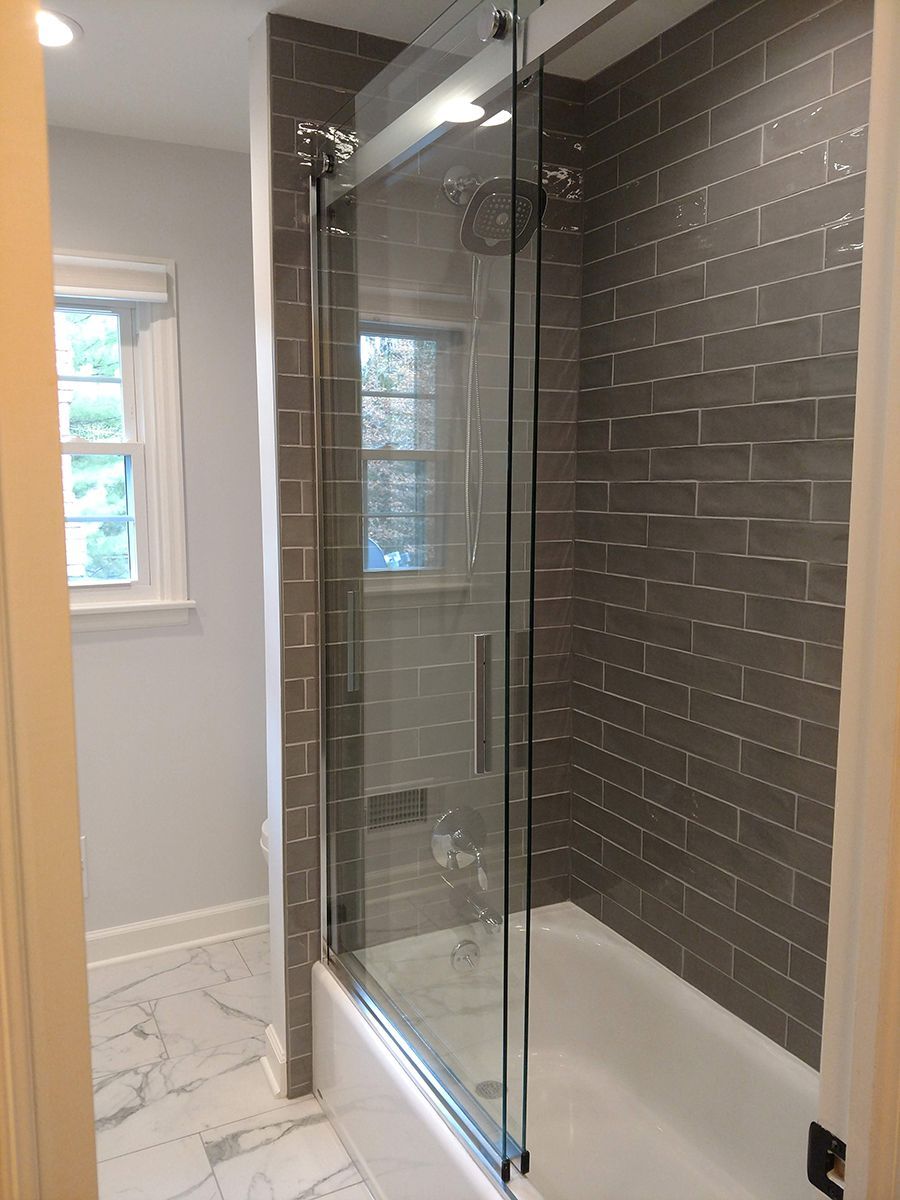Bathroom with gray subway tile shower surround, glass door, and white tub.