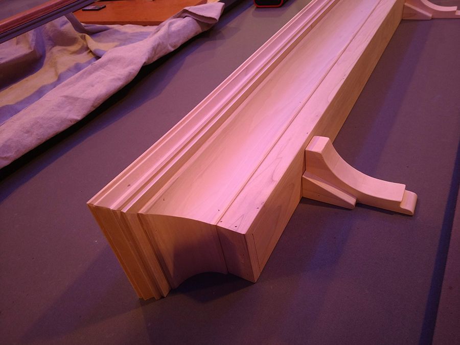 Wooden architectural molding, light brown with decorative carvings, on a purple surface.