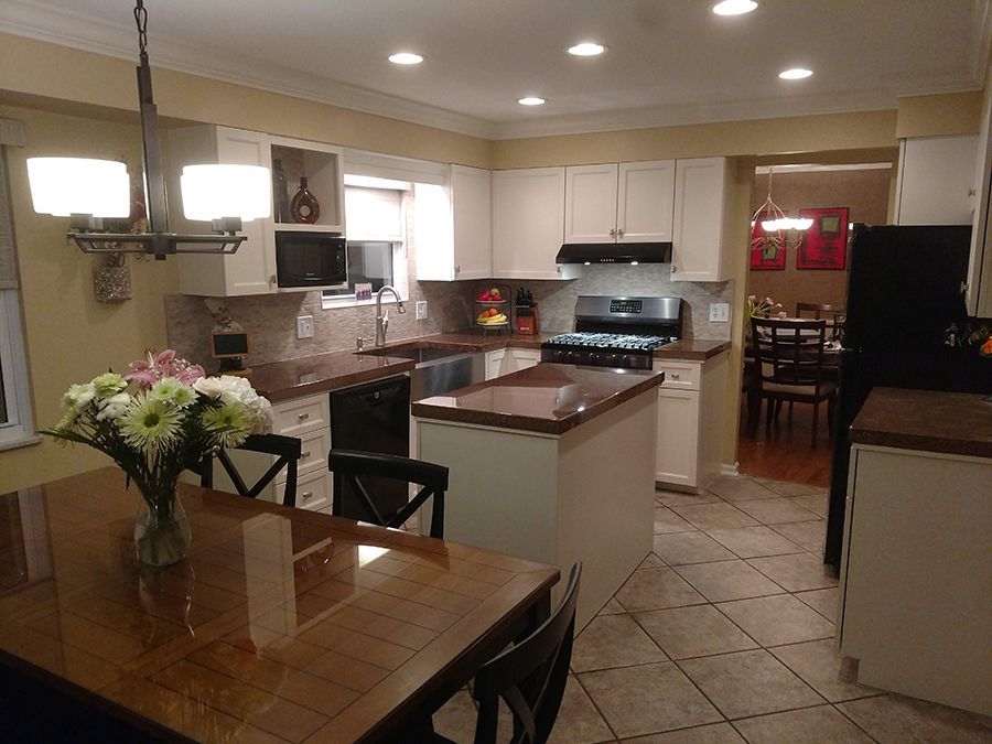 Kitchen with white cabinets, island, and dining table; countertops are brown, and floors are tiled.