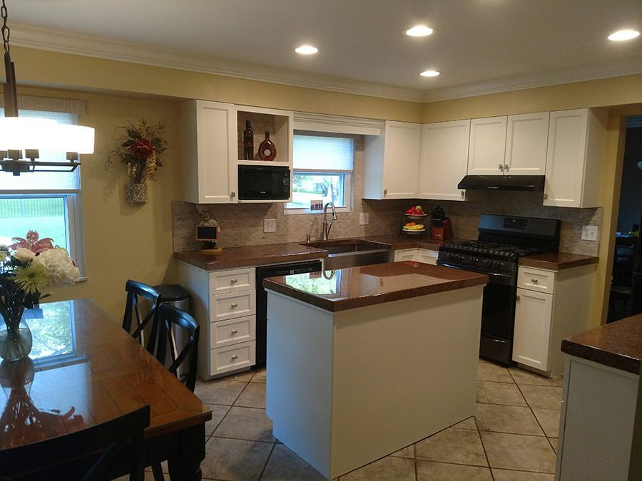 Kitchen with white cabinets, dark countertops, island, and dining table; yellow walls and tile floor.