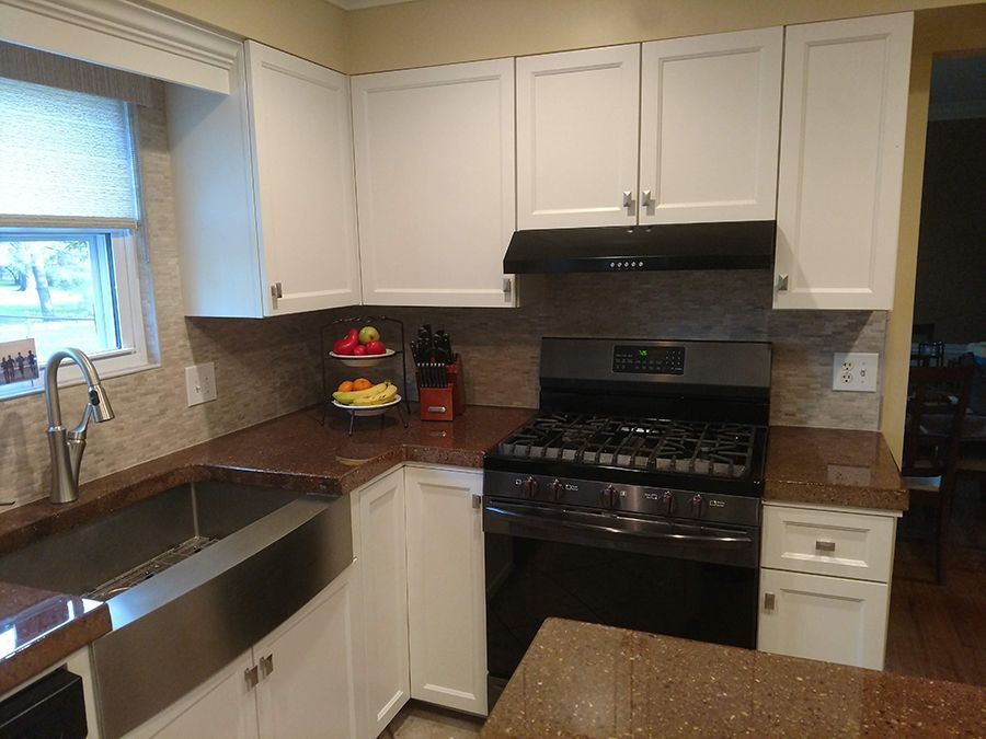 White kitchen cabinets, brown countertops, and a stainless steel sink with a dark stove and vent hood.